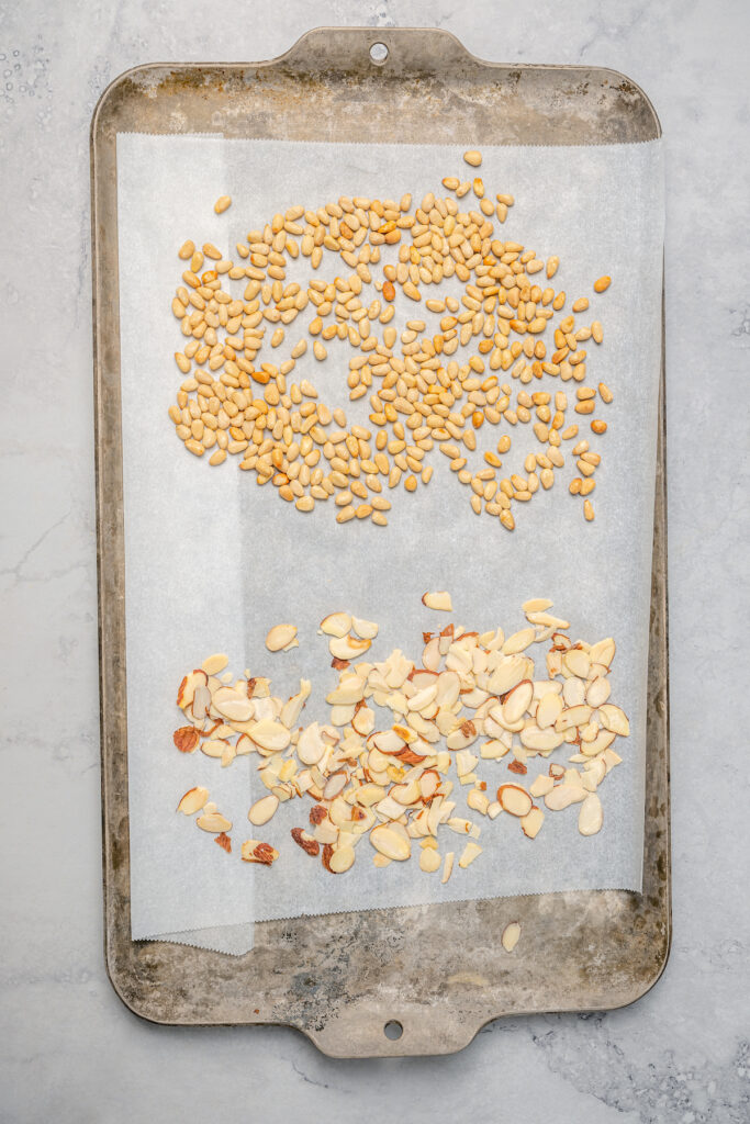 Toasting pine nuts and almonds on a baking sheet.