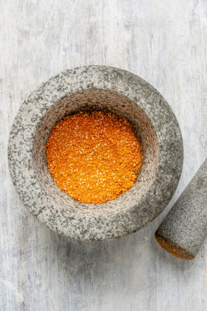 A mortar and pestle with chile powder, ground sesame seeds, and fleur de sel.