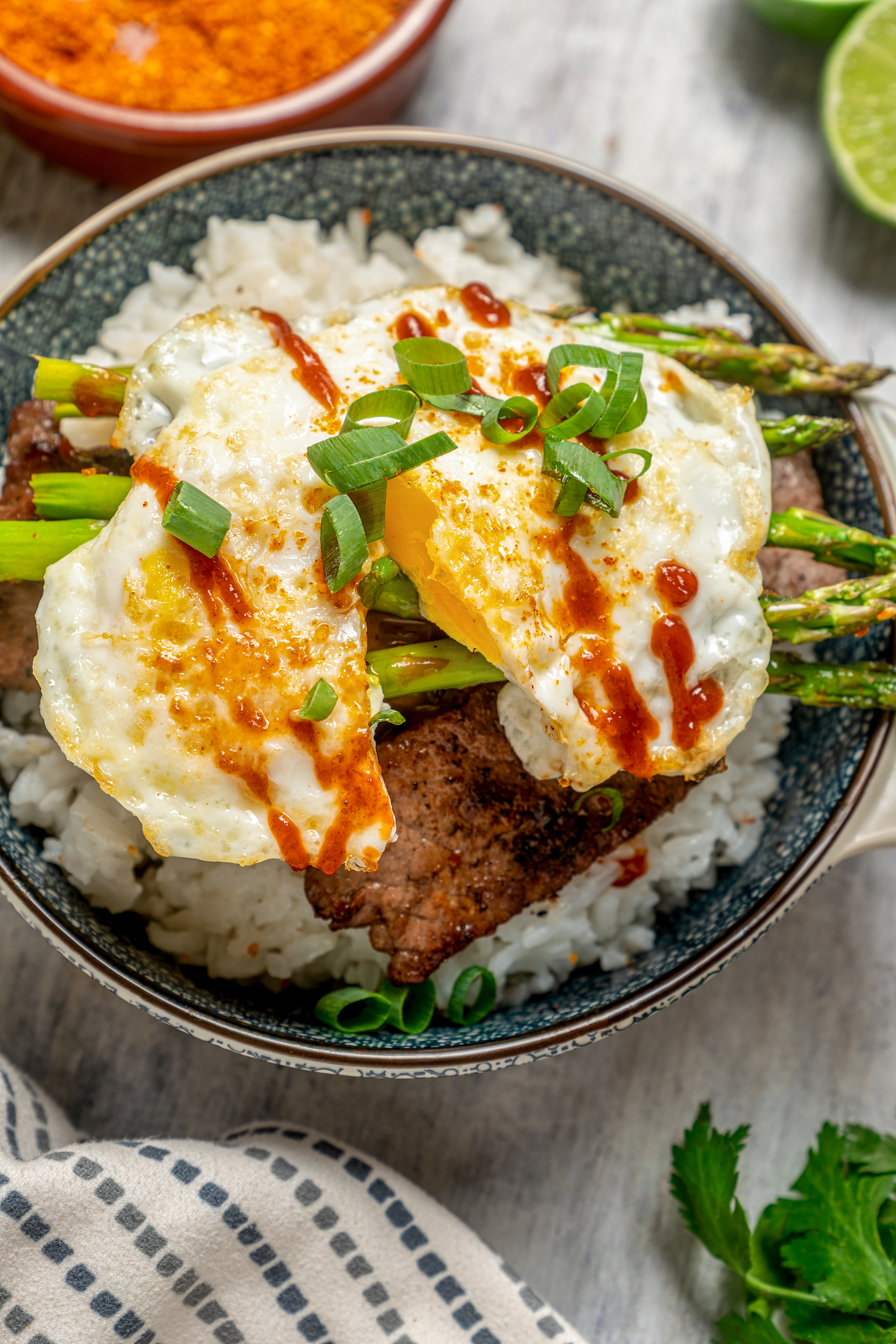 A fried egg, cut in half, on top of a rice bowl with steak.