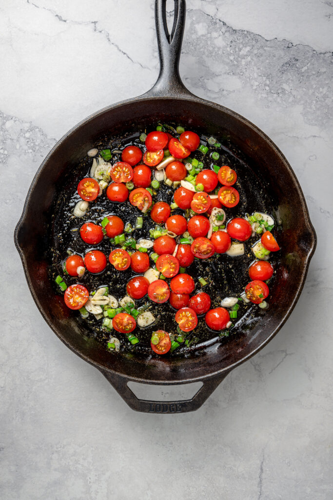 Tomatoes and aromatics cooking in a skillet.