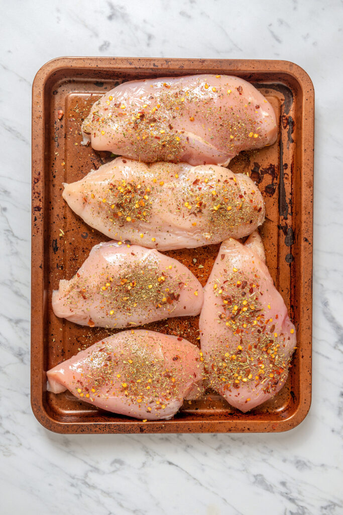 Seasoned raw chicken breast on a tray.