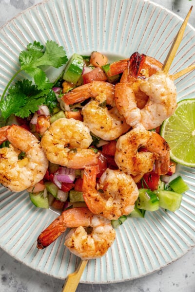 Grilled shrimp on wooden skewers served with fresh veggies and a lime wedge.