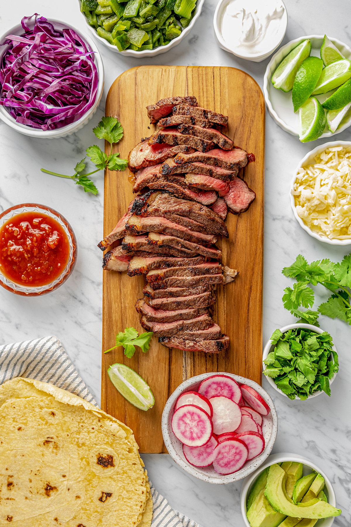 Grilled steak on a cutting board, surrounded by dishes of toppings.