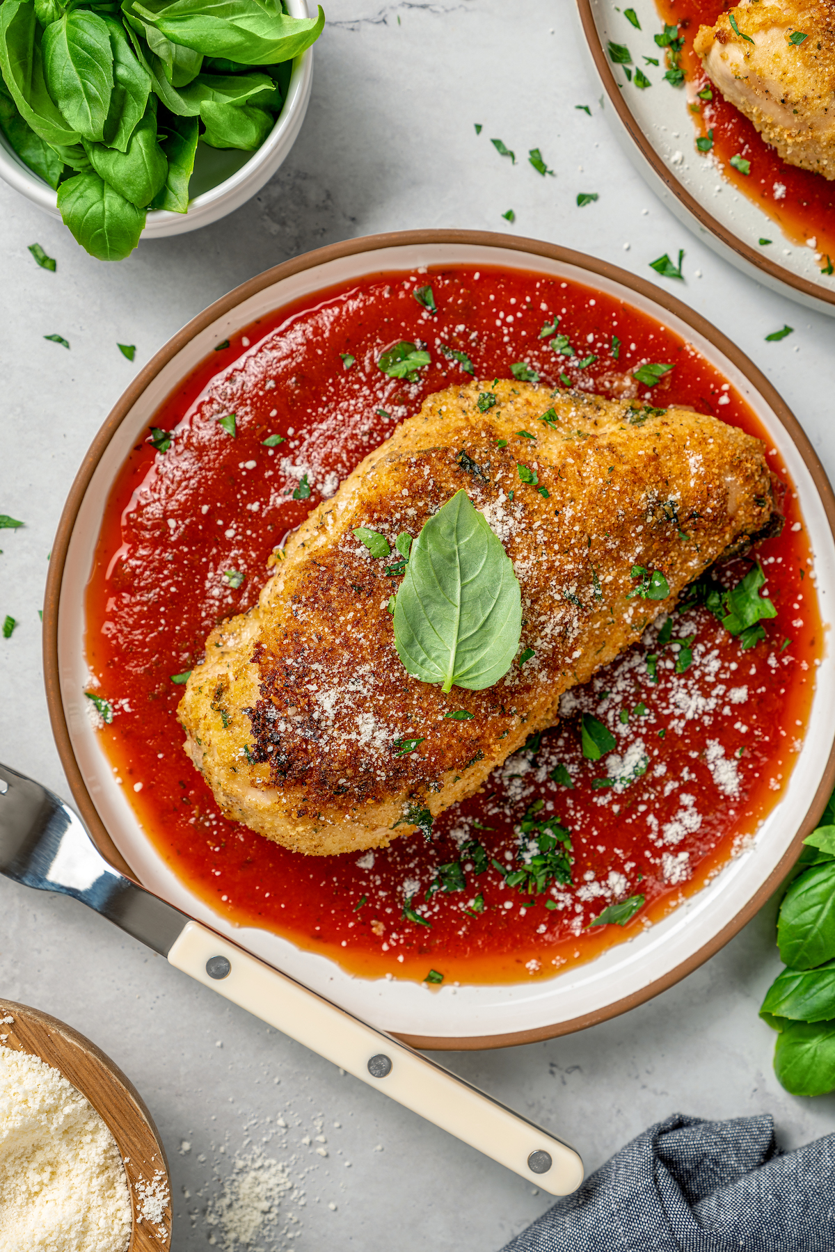 A plate of marinara with a breaded chicken breast on top, garnished with basil.