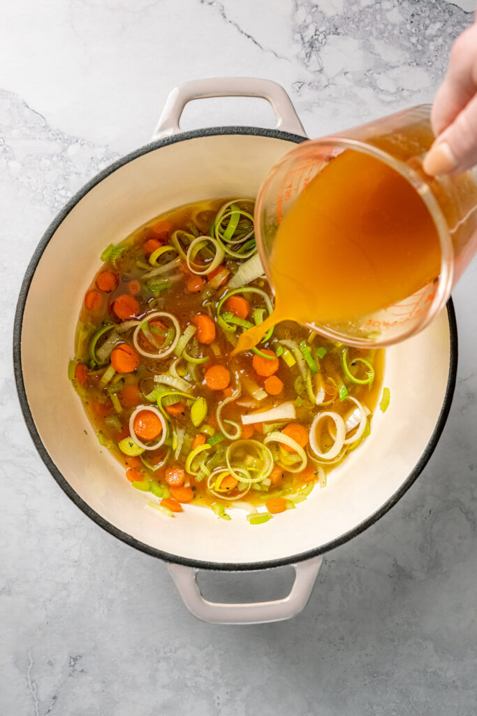 Pouring vegetable broth over vegetables in a pot.