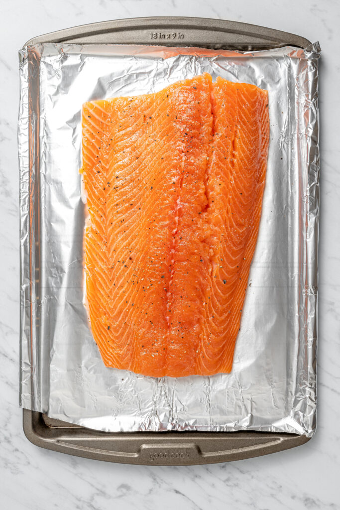 Seasoned raw salmon on a foil-lined tray.