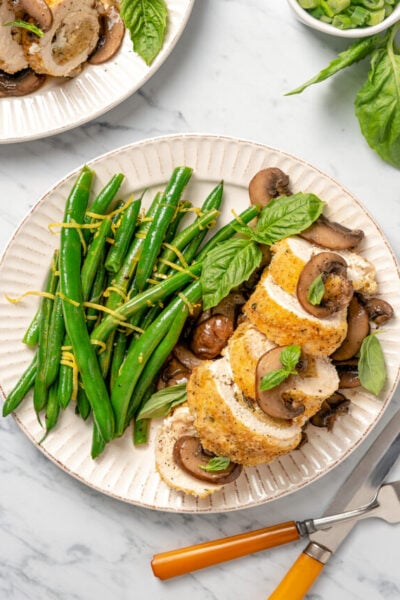 A dinner plate with a sliced stuffed chicken breast and lemony green beans.