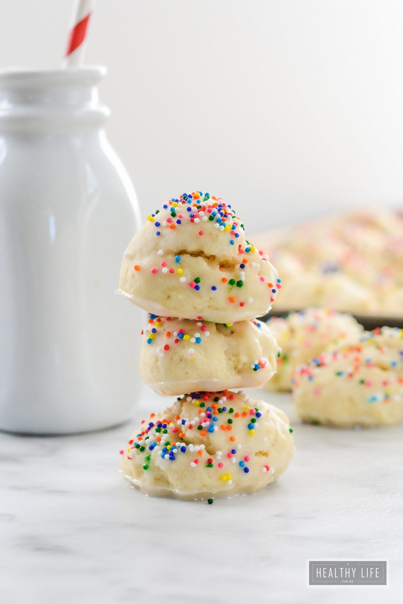 A couple of stacked anisette cookies with a jug of milk in the background.