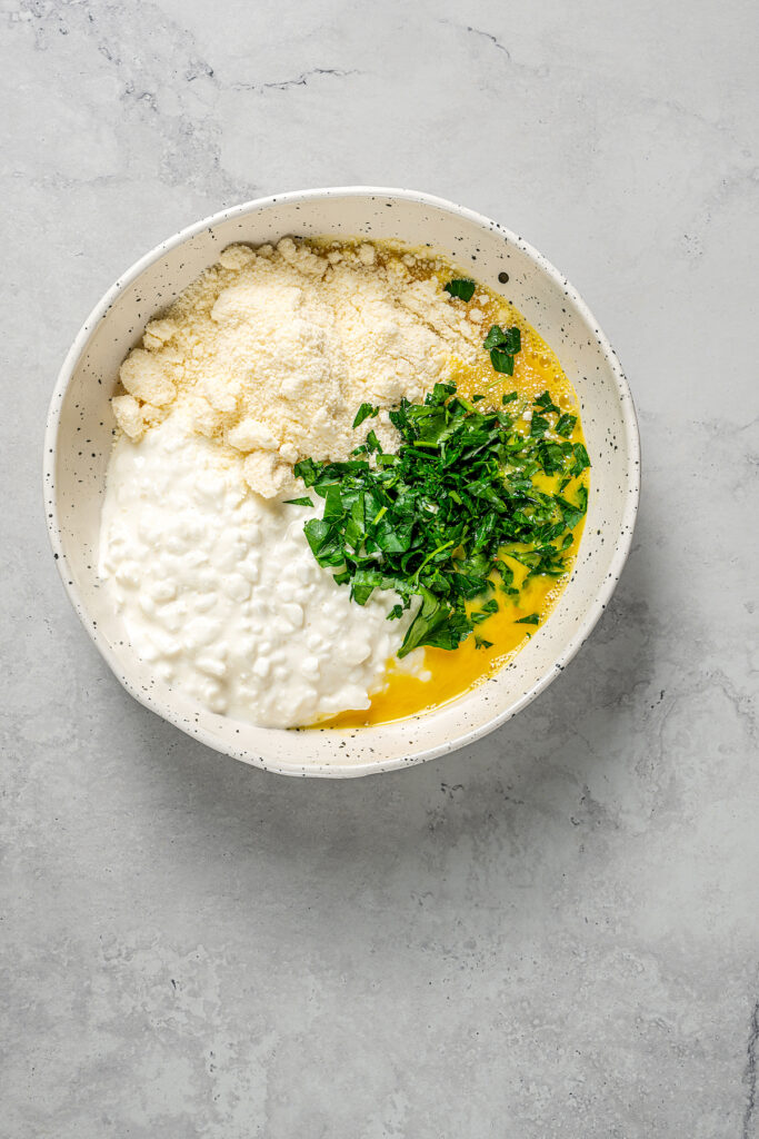 Cottage cheese, parmesan, eggs, and parsley in a bowl.