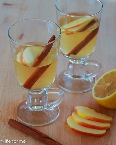 Two hot toddy recipes in glasses with apple slices and cinnamon sticks.