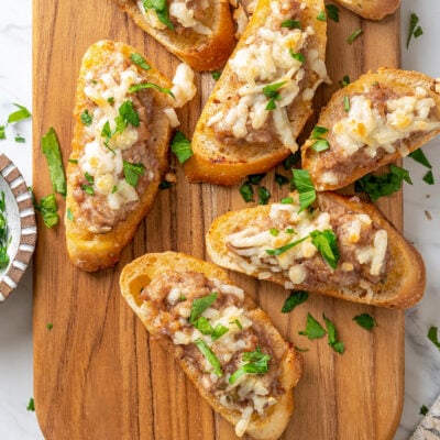 A cutting board with warm sausage crostini.