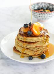 Drizzling syrup onto stack of paleo peach pancakes