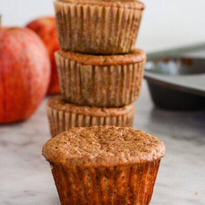 Apple pie protein muffins next to fresh apples.