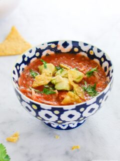 Soup in a bowl with avocado, cilantro, and tortilla chips.