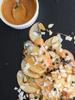 Apple nachos on a black surface with a bowl of melted almond butter beside them