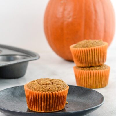 Pumpkin protein muffins, two in the background and one on a plate.