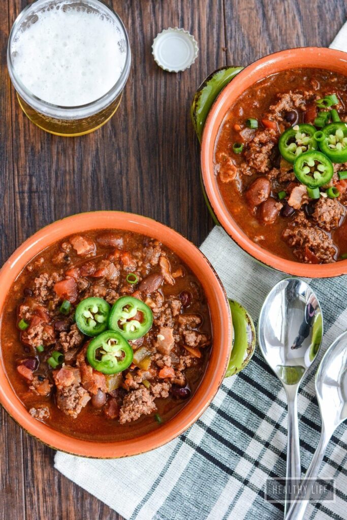 Overhead shot of chili in bowls with small mason jars of beer.