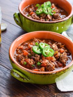Green earthenware bowls of bison chili on a wooden table.