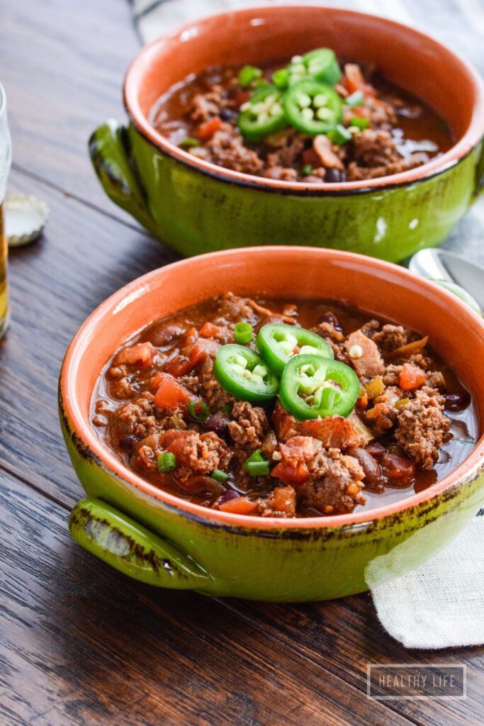 Green earthenware bowls of bison chili on a wooden table.