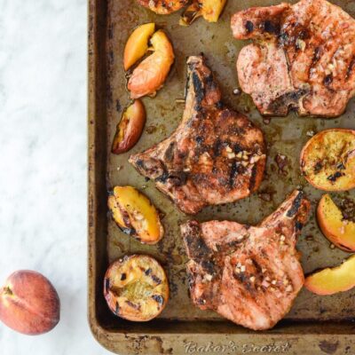 Overhead view of grilled pork chops and peaches on sheet pan
