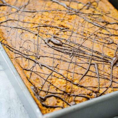 A cooled pumpkin protein cake in a pan with melted chocolate drizzled on top of it