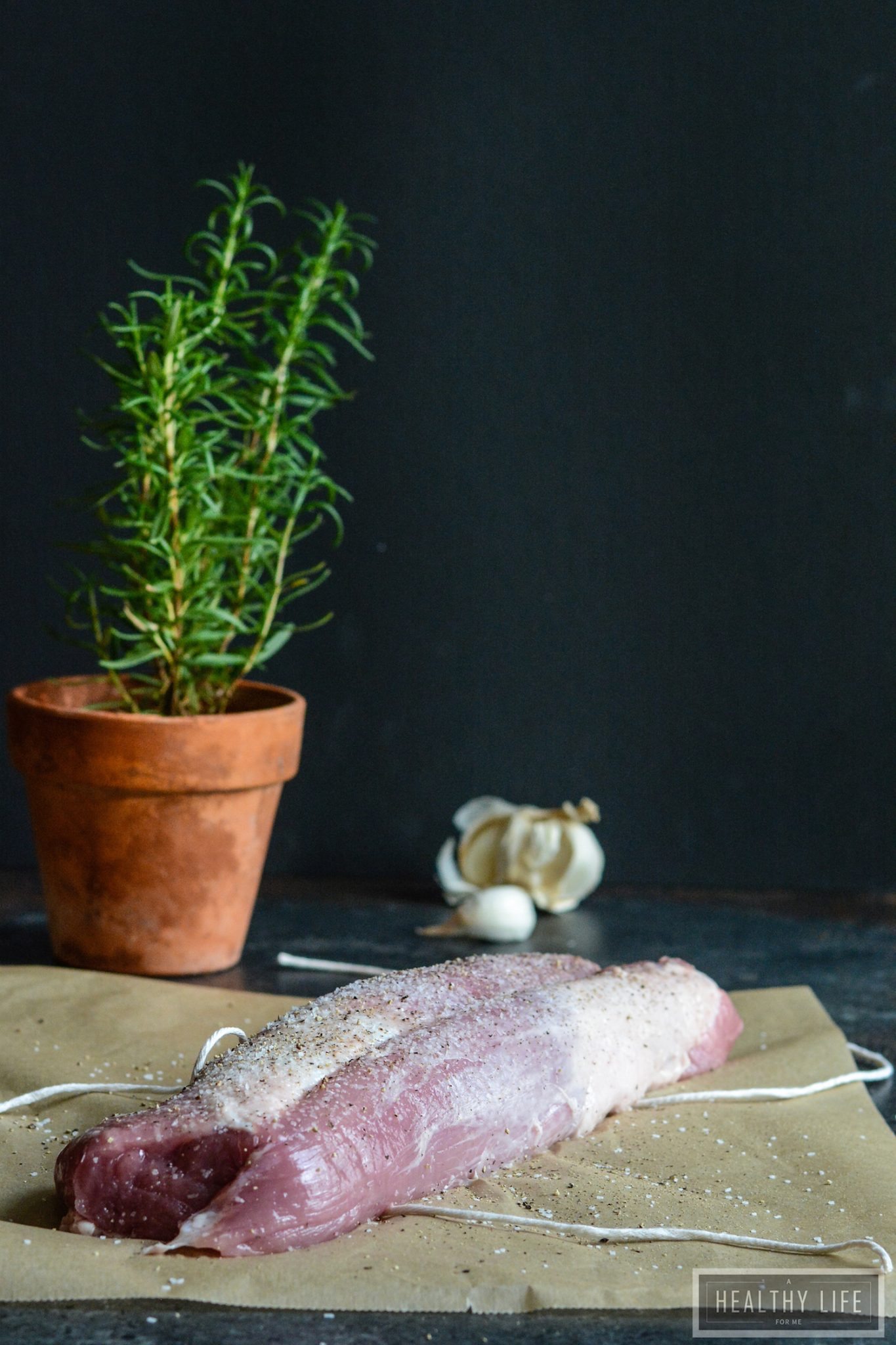 Raw pork tenderloin in front of a rosemary plant