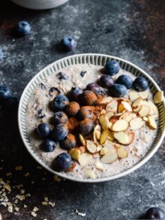 Bowl of blueberry overnight oats topped with more blueberries, sliced almonds, and cinnamon.