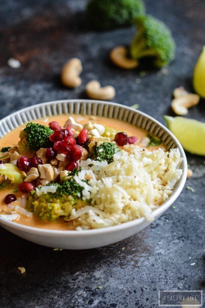 A bowl of curry chicken with cauliflower rice and pomegranate arils.