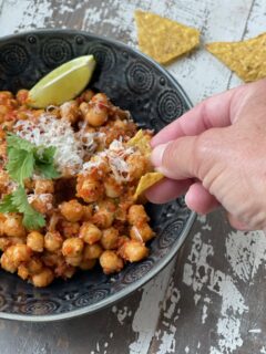 A hand dipping a tortilla chip into a bowl of chickpeas in sofrito