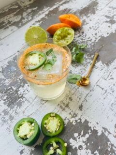 Spicy jalapeno margarita in a glass next to lime wedges.