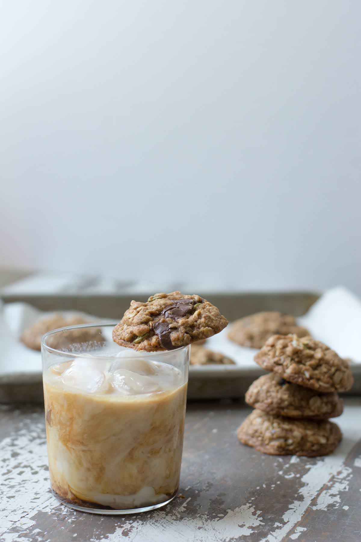 Trail mix cookie set on rim of iced coffee glass, next to stack of cookies