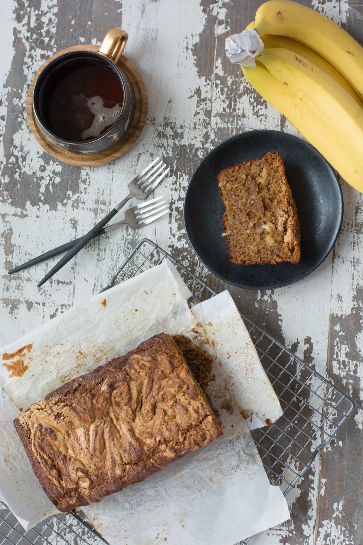 A loaf of banana bread beside a mug of coffee and a single slice of bread on a plate