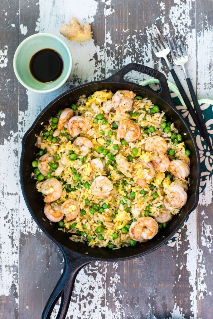 Shrimp fried rice in a cast-iron skillet beside a small bowl of soy sauce and two forks