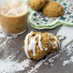 Two glazed pumpkin oatmeal cookies in front of a cup of pumpkin cold brew