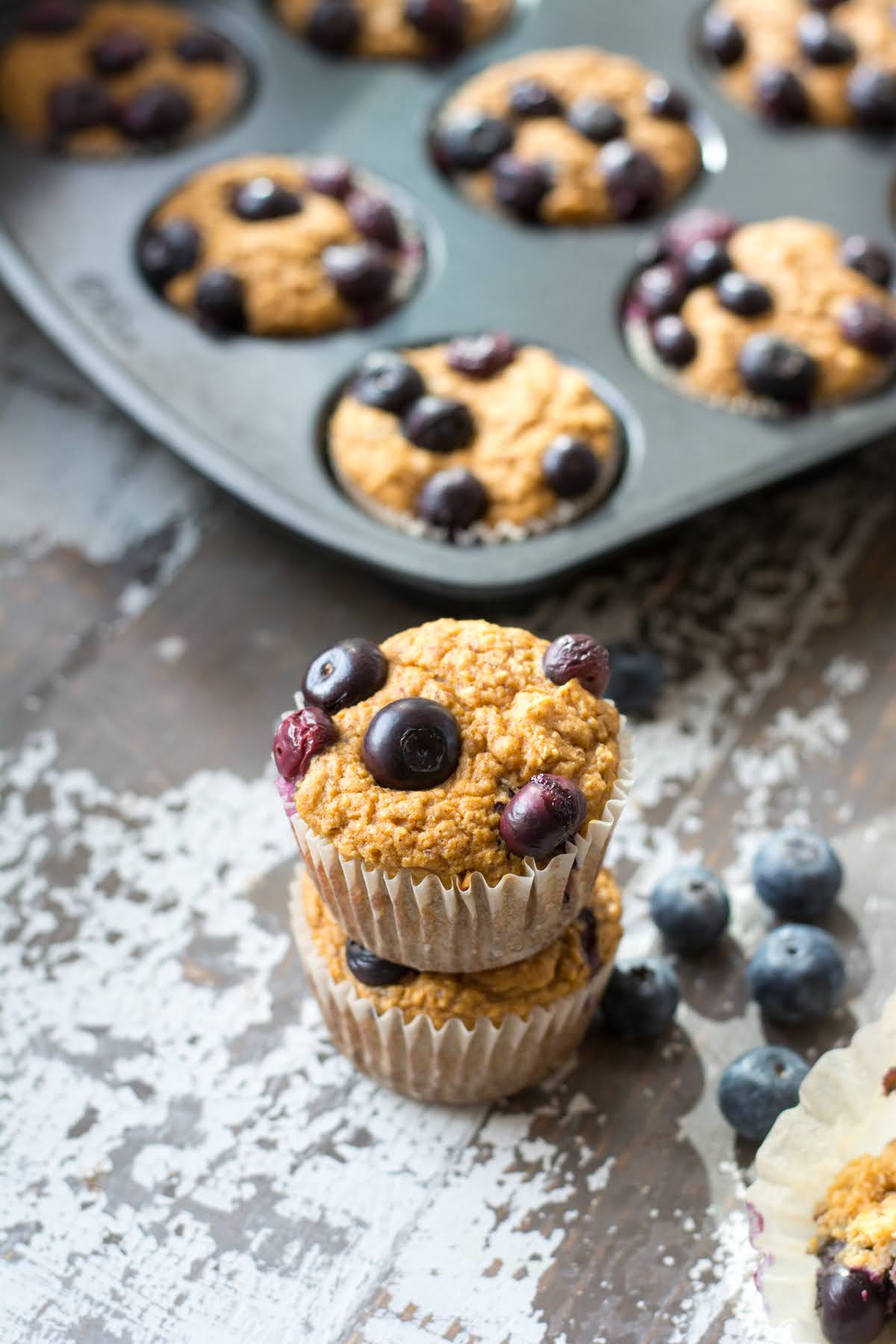 Two blueberry muffins stacked together in front of a muffin tin