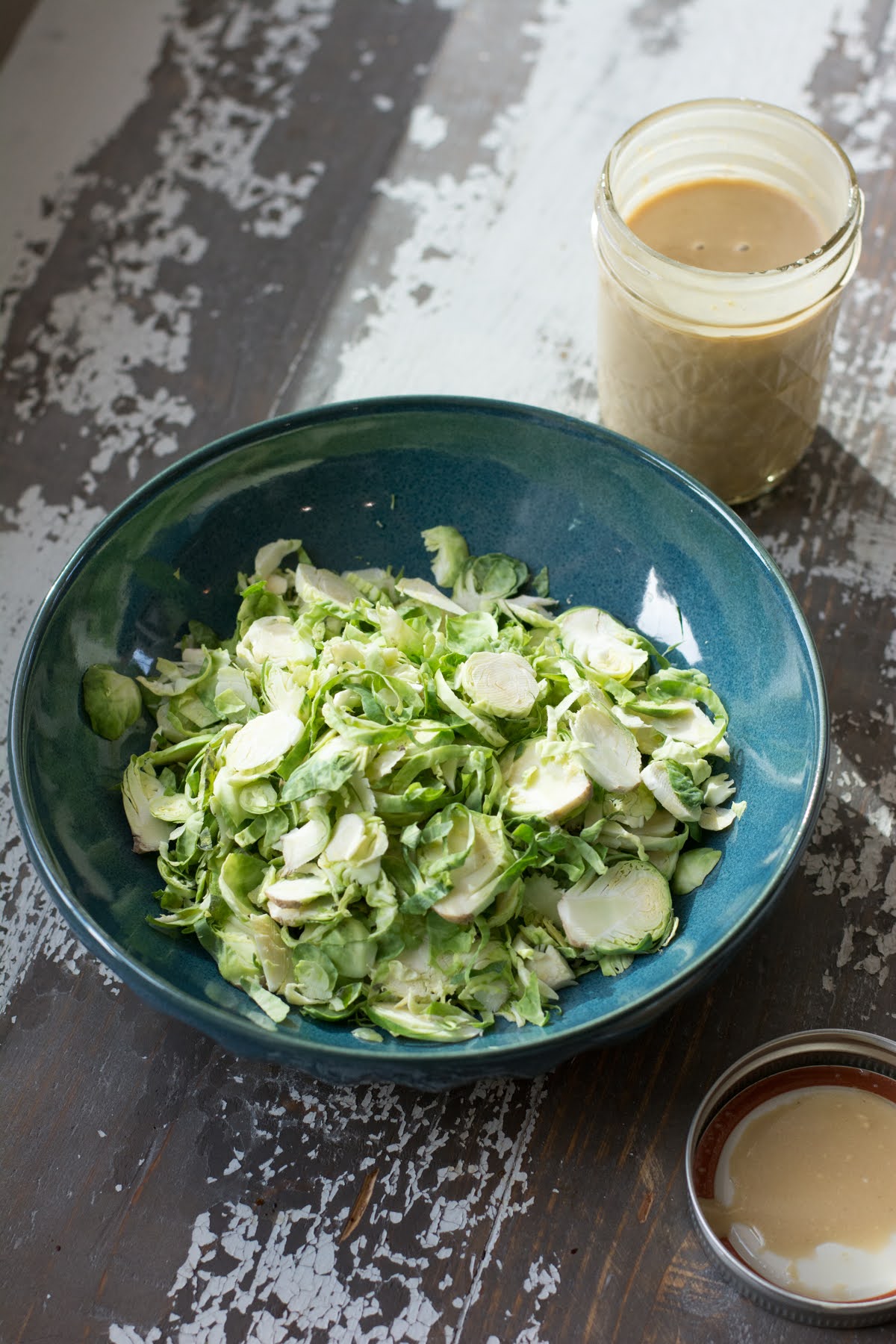 A bowl of thinly sliced brussels sprouts next to a jar od vinaigrette