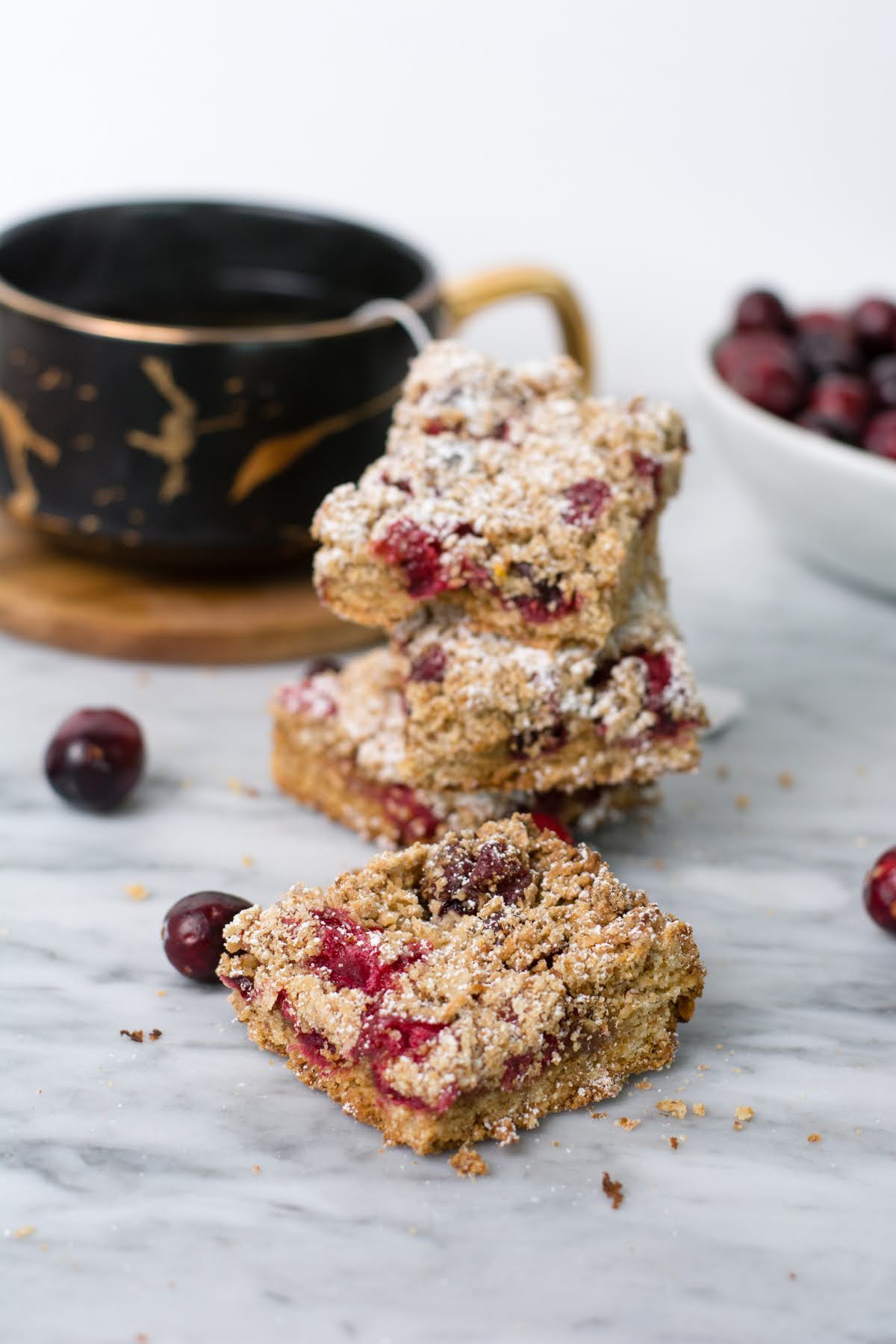 Several cranberry crumble bars stacked up with a cup of coffee.