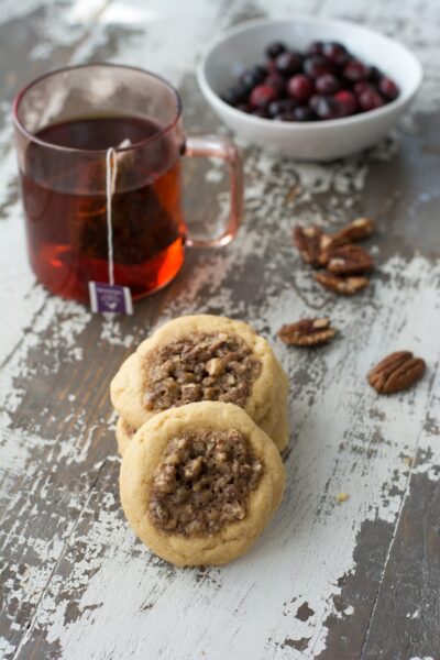 Pecan pie cookies with a cup of tea and bowl of cranberries on a table.