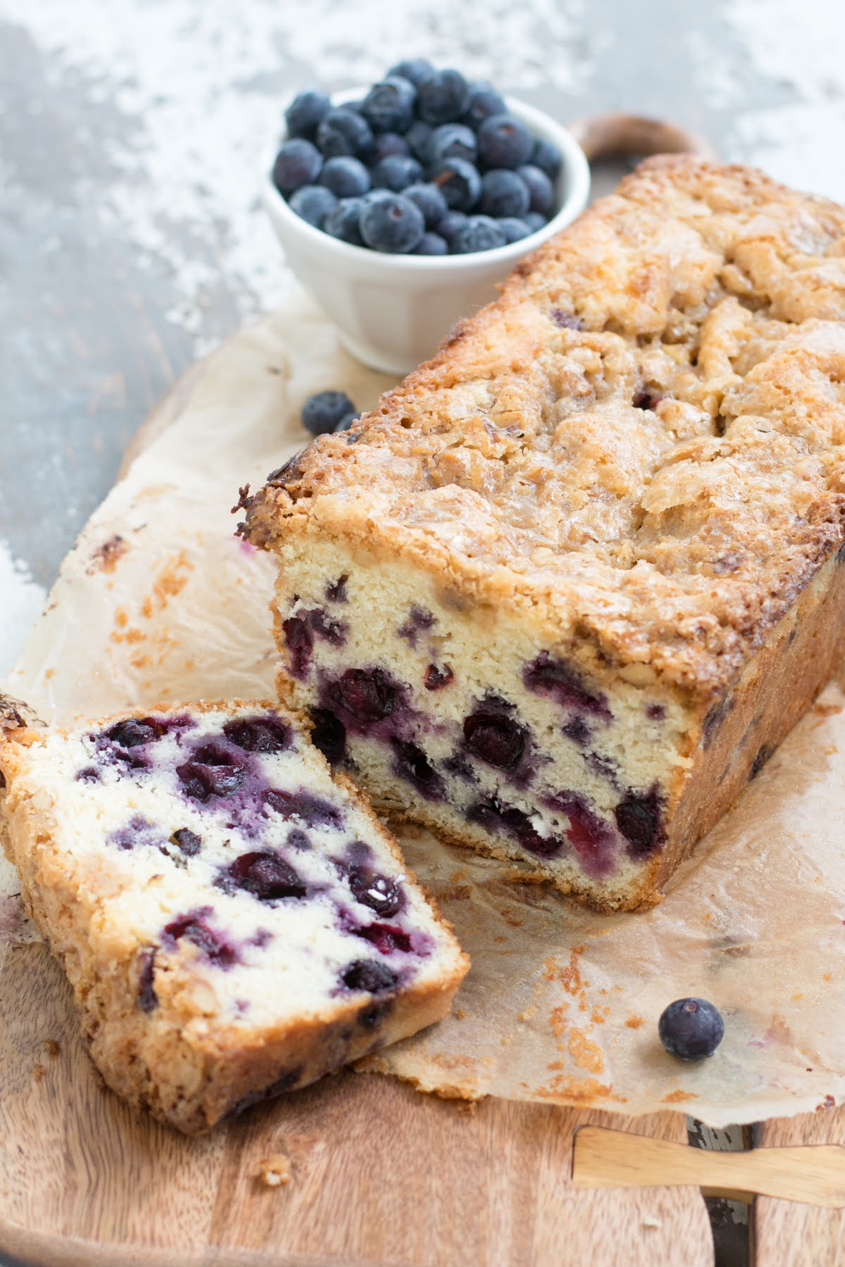 A blueberry loaf cake next to a cup of fresh blueberries.