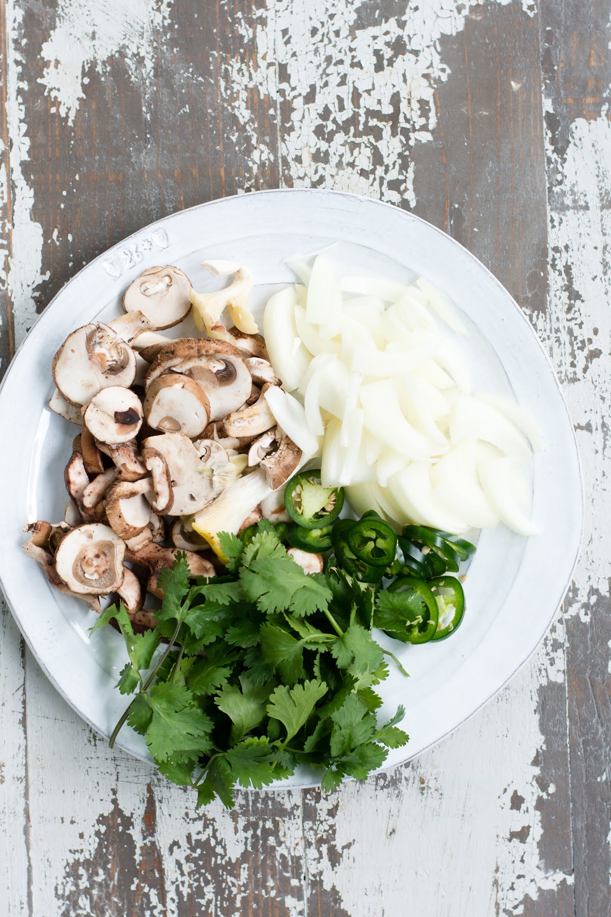 Onions, mushrooms, chilis, and cilantro on a plate.