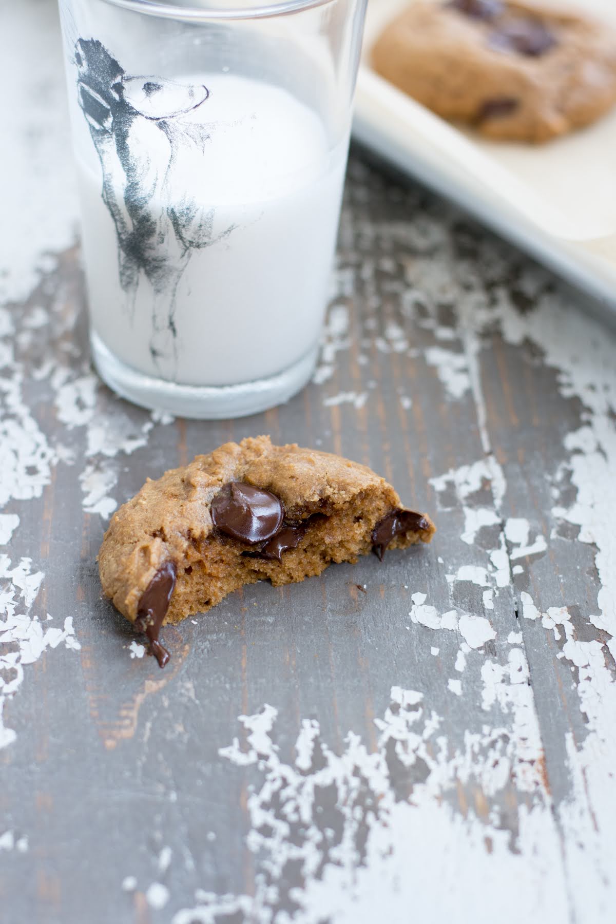 Half a protein cookie on a baking sheet next to a glass of milk.
