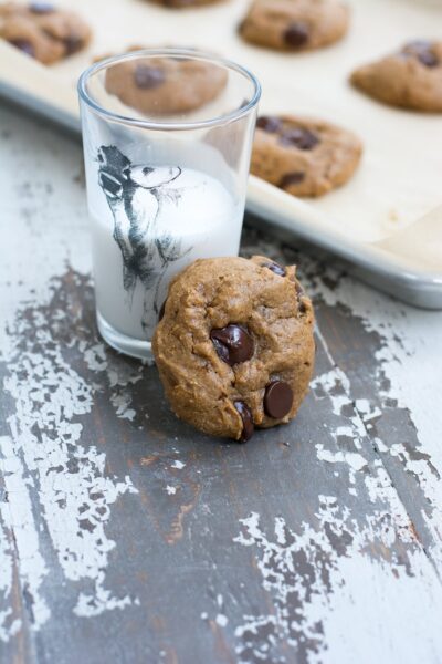 A protein cookie next to a glass of milk and a baking sheet of additional cookies.