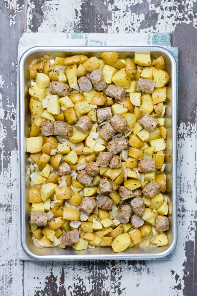 Sausage pieces added to sheet pan of potatoes and onions.
