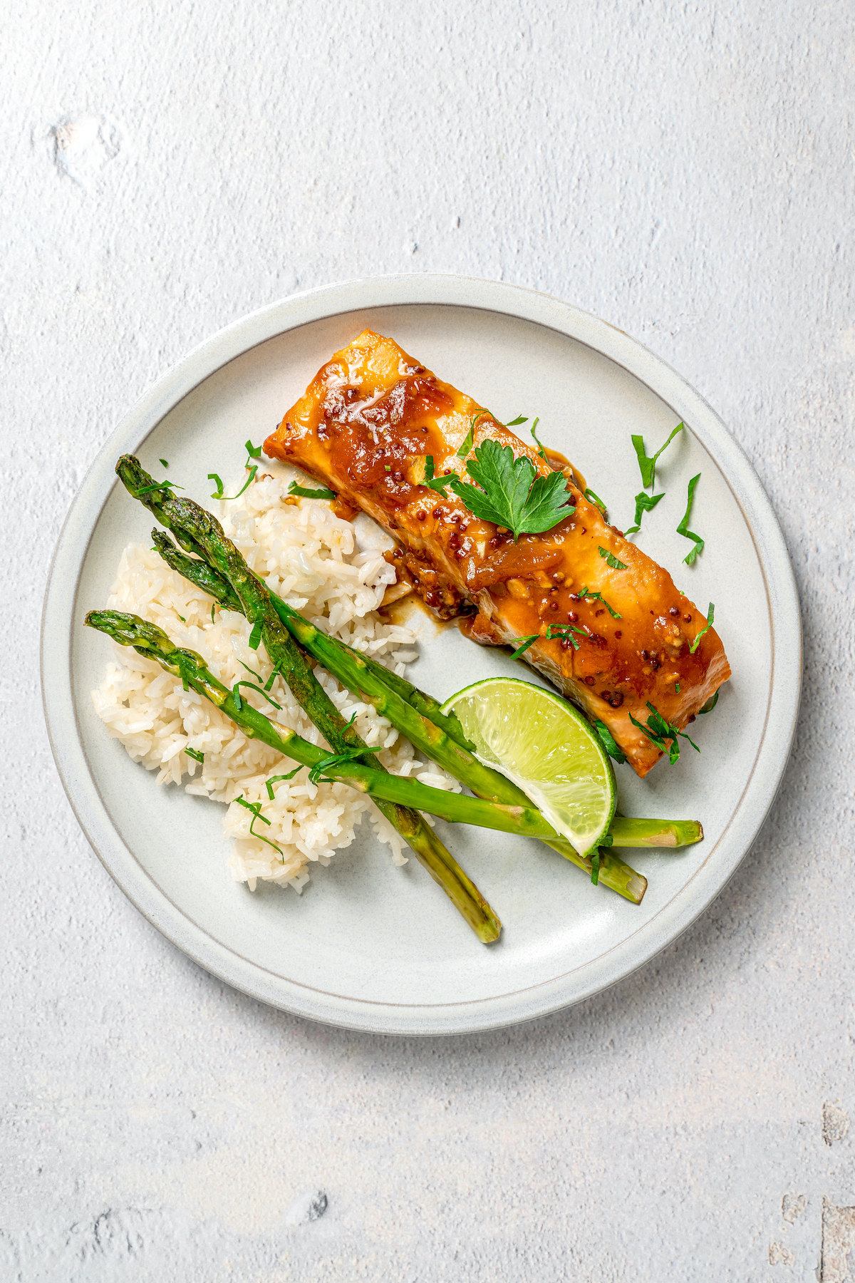 A dinner plate with rice, asparagus, salmon, and a lime wedge.