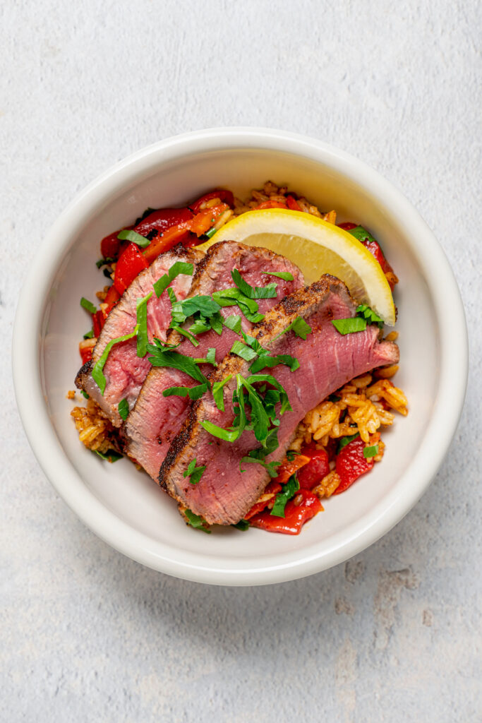Sliced steak served over seasoned rice with peppers.