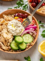 A fork resting in a bowl of quinoa, chicken, vegetables, and salad.