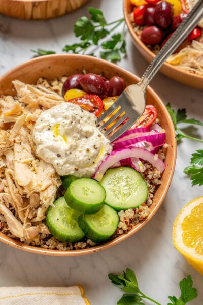 A fork resting in a bowl of quinoa, chicken, vegetables, and salad.