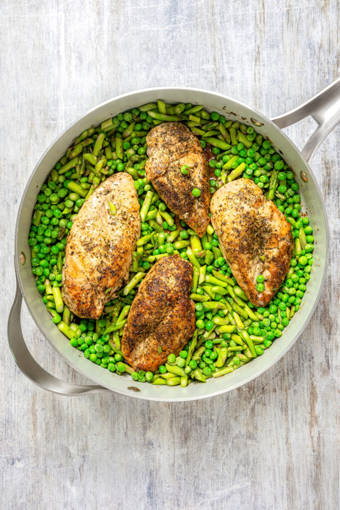 Chicken in a skillet with peas and asparagus.