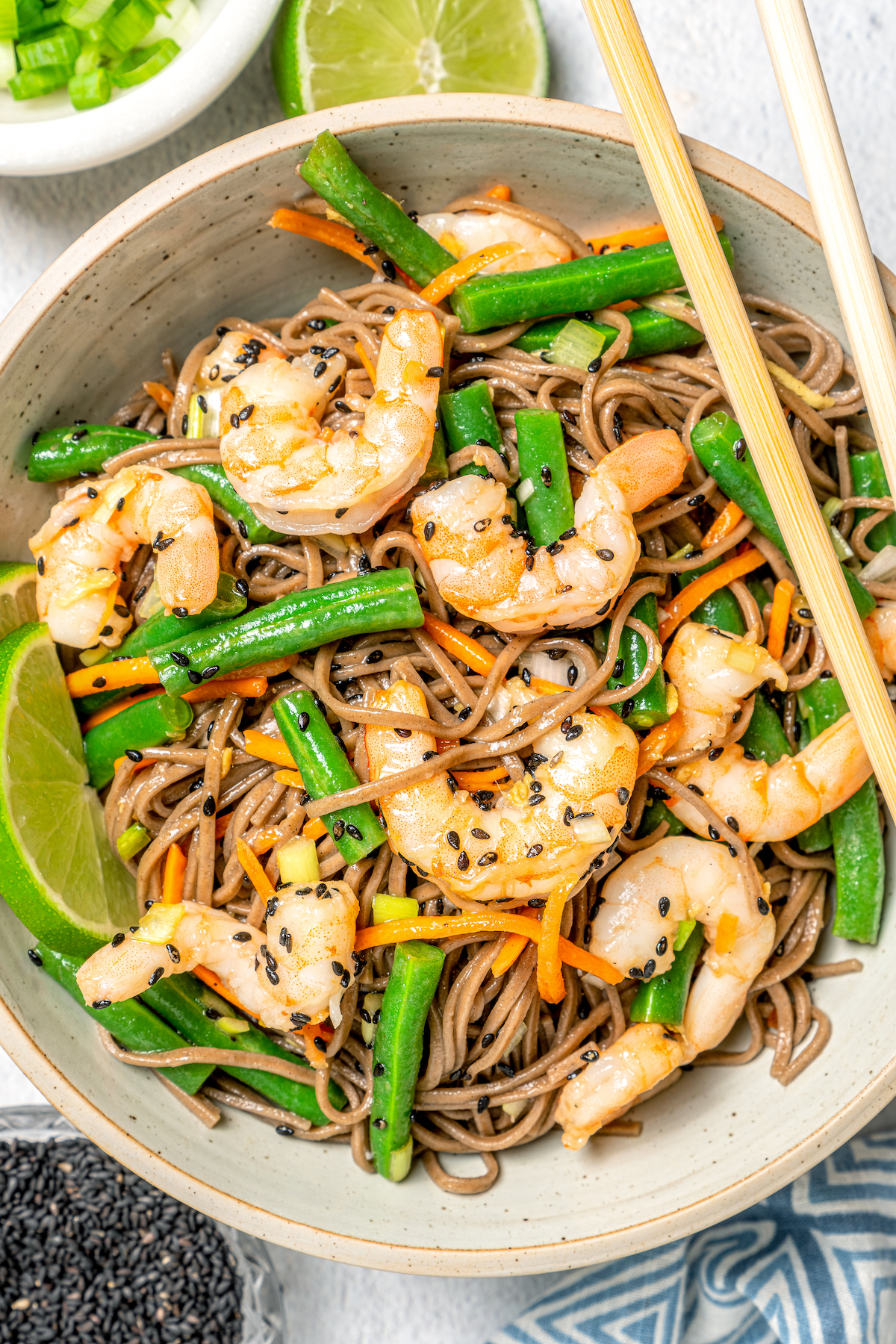 A bowl of soba noodles with shrimp, with a pair of chopsticks.