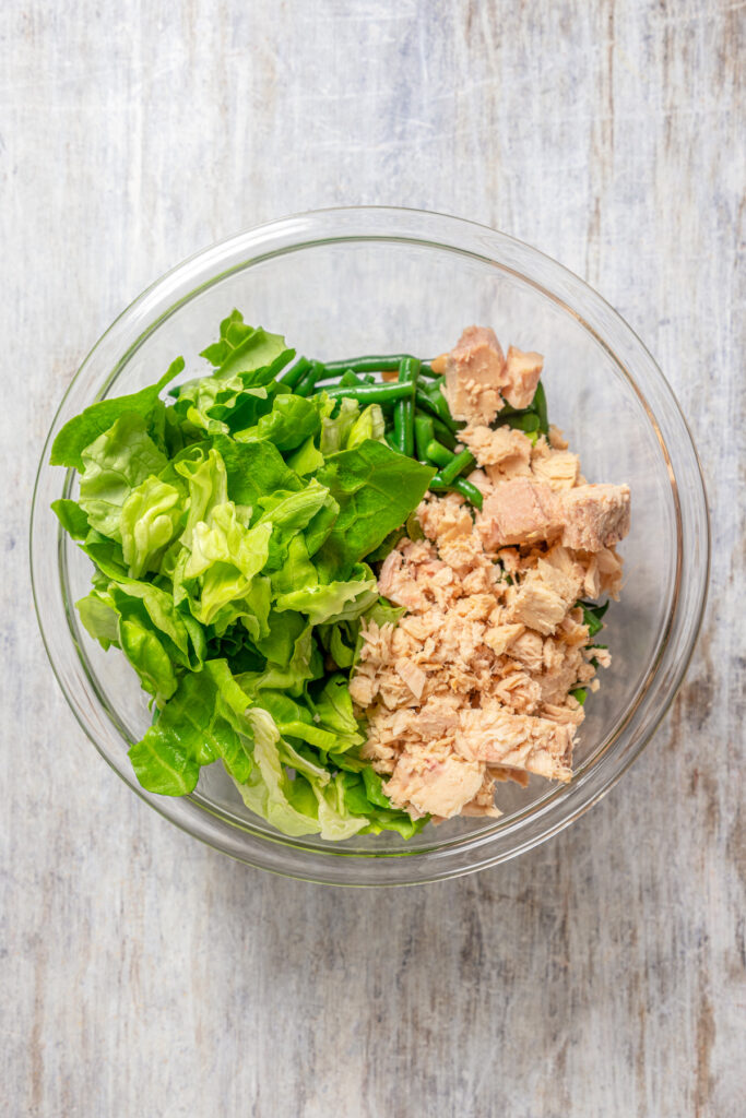 Lettuce and tuna added to a salad bowl.